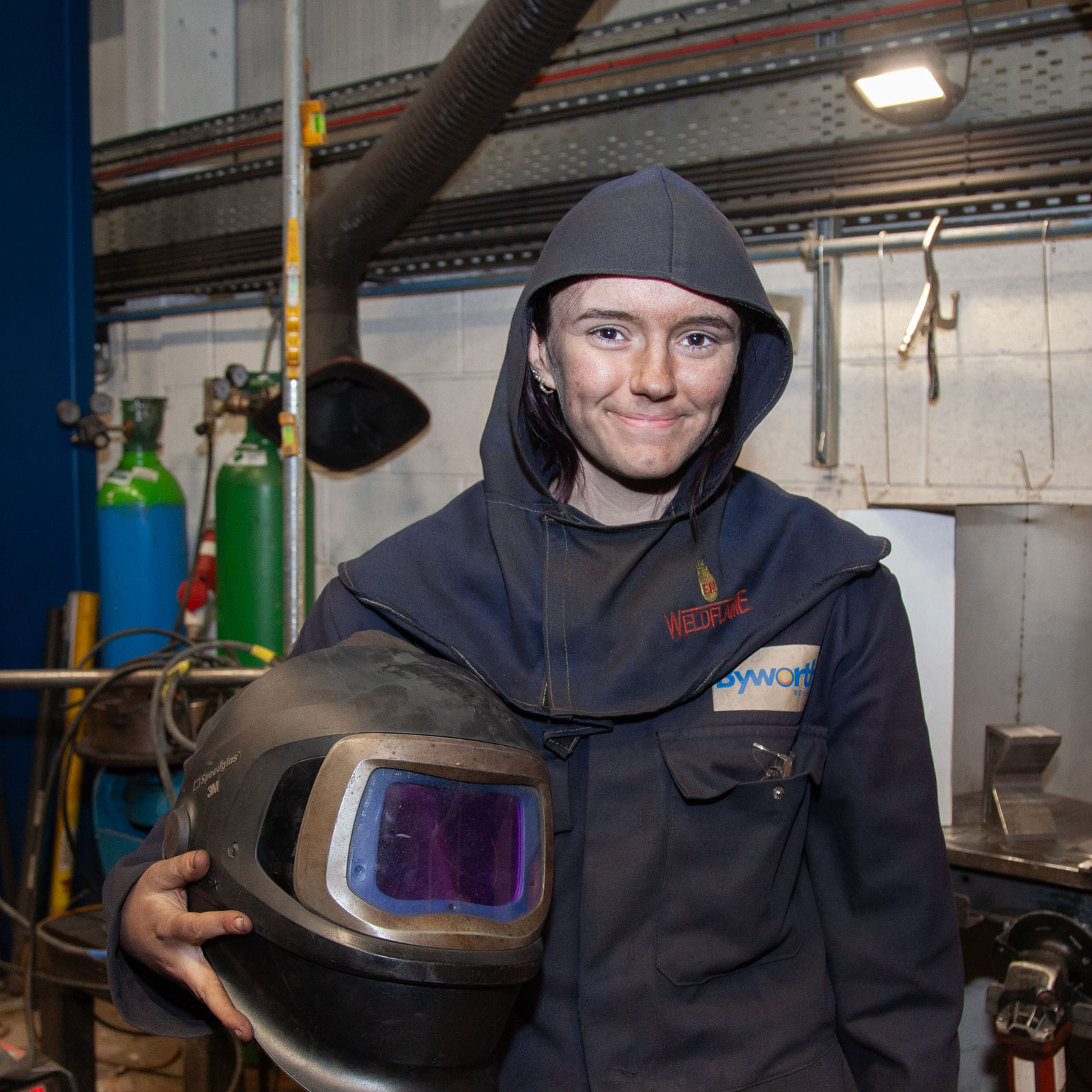 A woman stood smiling with a welding mask under her arm 